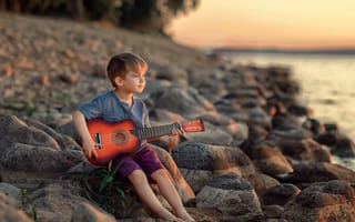 Картинка Маленький мальчик сидит с гитарой на камнях у моря