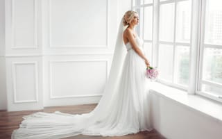 Картинка Красивая девушка в белом свадебном платье с букетом стоит у окна