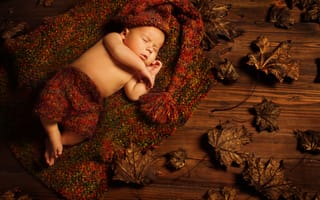 Картинка Маленький ребенок спит в вязаном костюме на полу с сухими листьями
