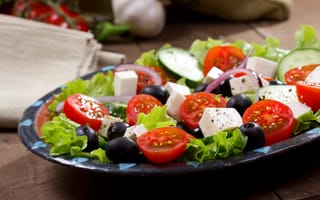 Картинка Салат с помидорами, огурцами, оливками, кусочками сыра и луком на листьях салата