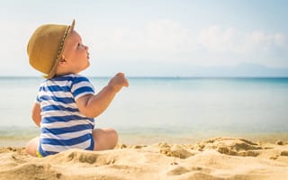 Картинка Маленький ребенок сидит на песке на пляже у моря