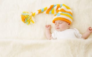 Картинка Маленький спящий под меховым покрывалом малыш в вязаной шапке