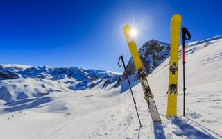 Картинка Лыжи с палками в заснеженных горах в лучах солнца