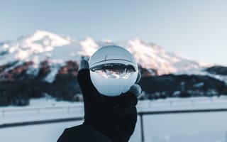 Обои Человек держит в руке стеклянный шар на фоне гор зимой