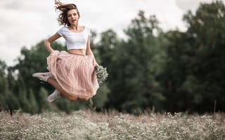 Картинка Красивая девушка в юбке прыгает на поле с ромашками