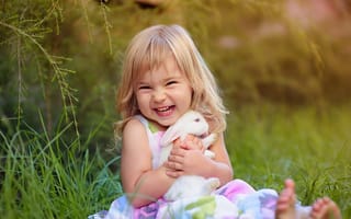 Картинка Довольная маленькая девочка обнимает белого кролика на траве