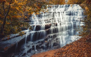 Обои Быстрая вода водопада стекает по каскадам камней осенью