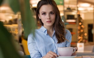 Картинка Девушка в голубой рубашке с чашкой кофе на столе в кафе