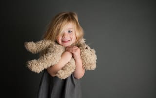Картинка Маленькая девочка с игрушечным медвежонком в руках на сером фоне