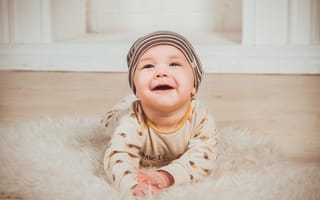 Картинка Улыбающийся грудной ребенок в шапке на полу