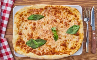 Картинка Пицца с сыром и листьями базилика на столе со столовыми приборами